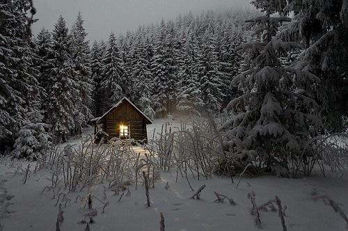 Mökki iltahämärässä keskellä lumista metsää